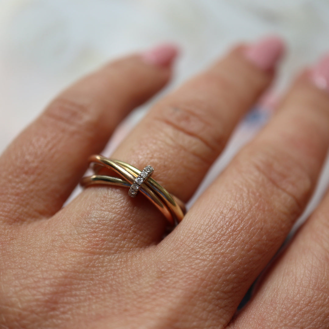 Gold multi bands ring with diamonds on a person's finger against a blurred background