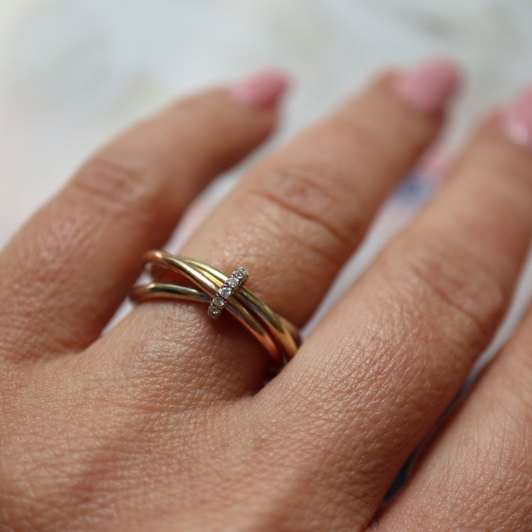 Gold multi bands ring with diamonds on a person's finger against a blurred background