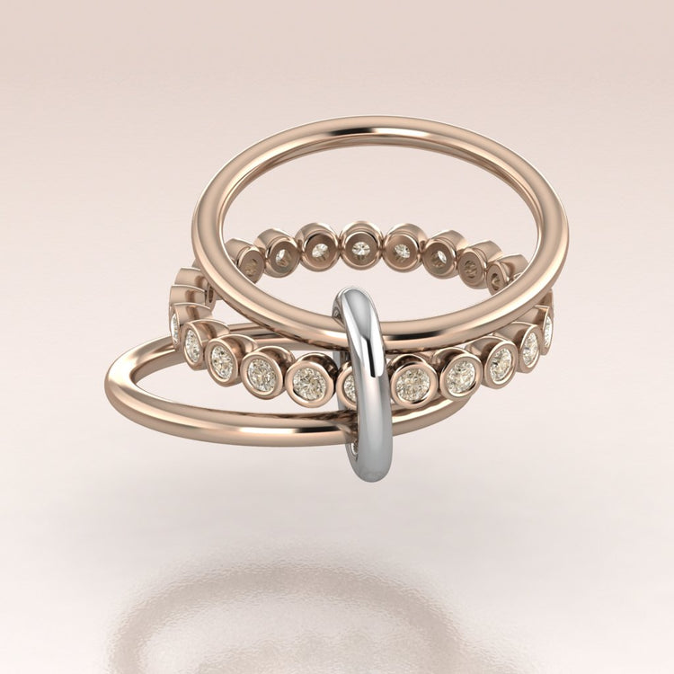 Set of three rose gold rings with diamond accents on a light pink background