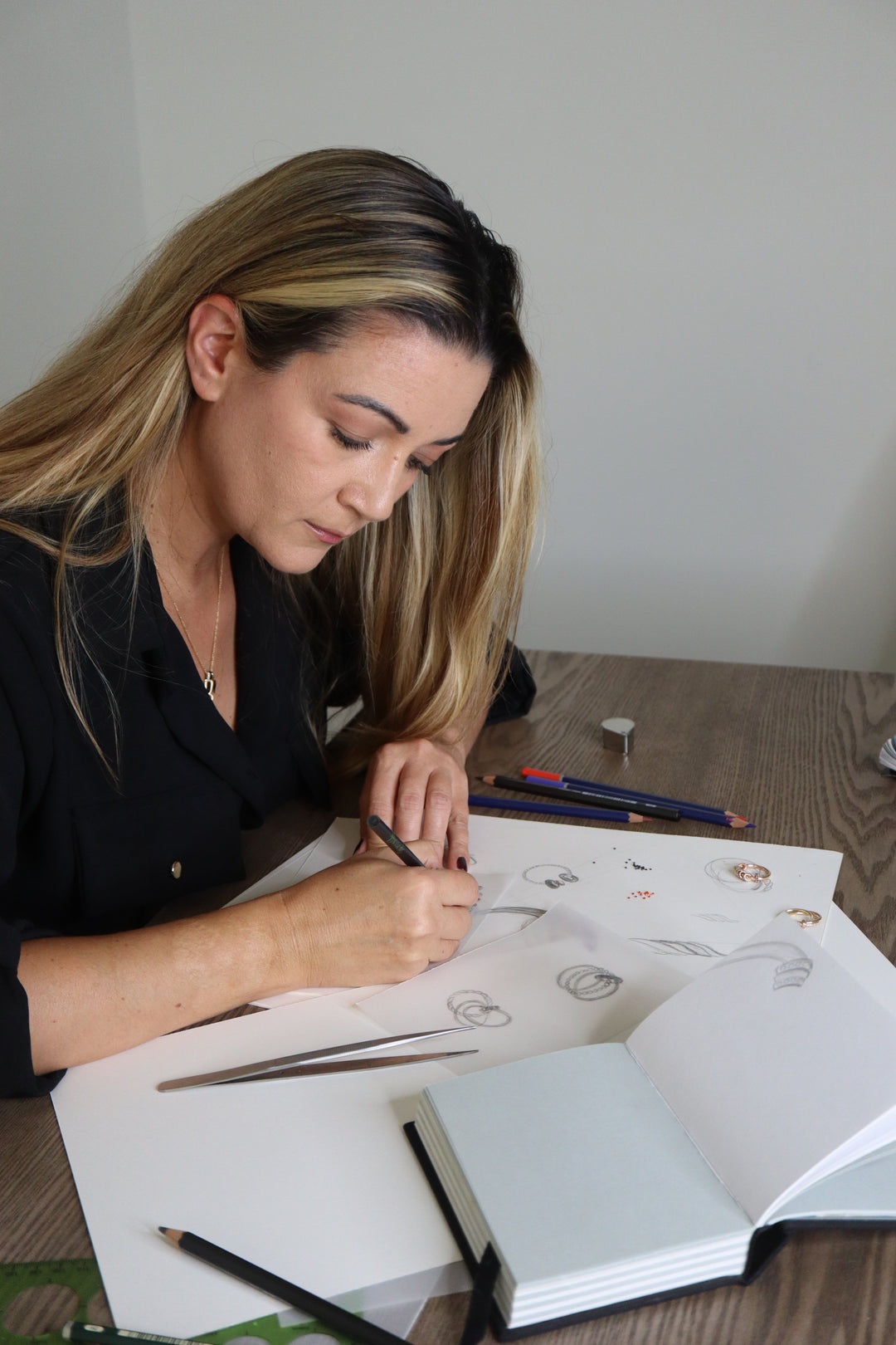 Woman drawing in a sketchbook with pencils on a table.