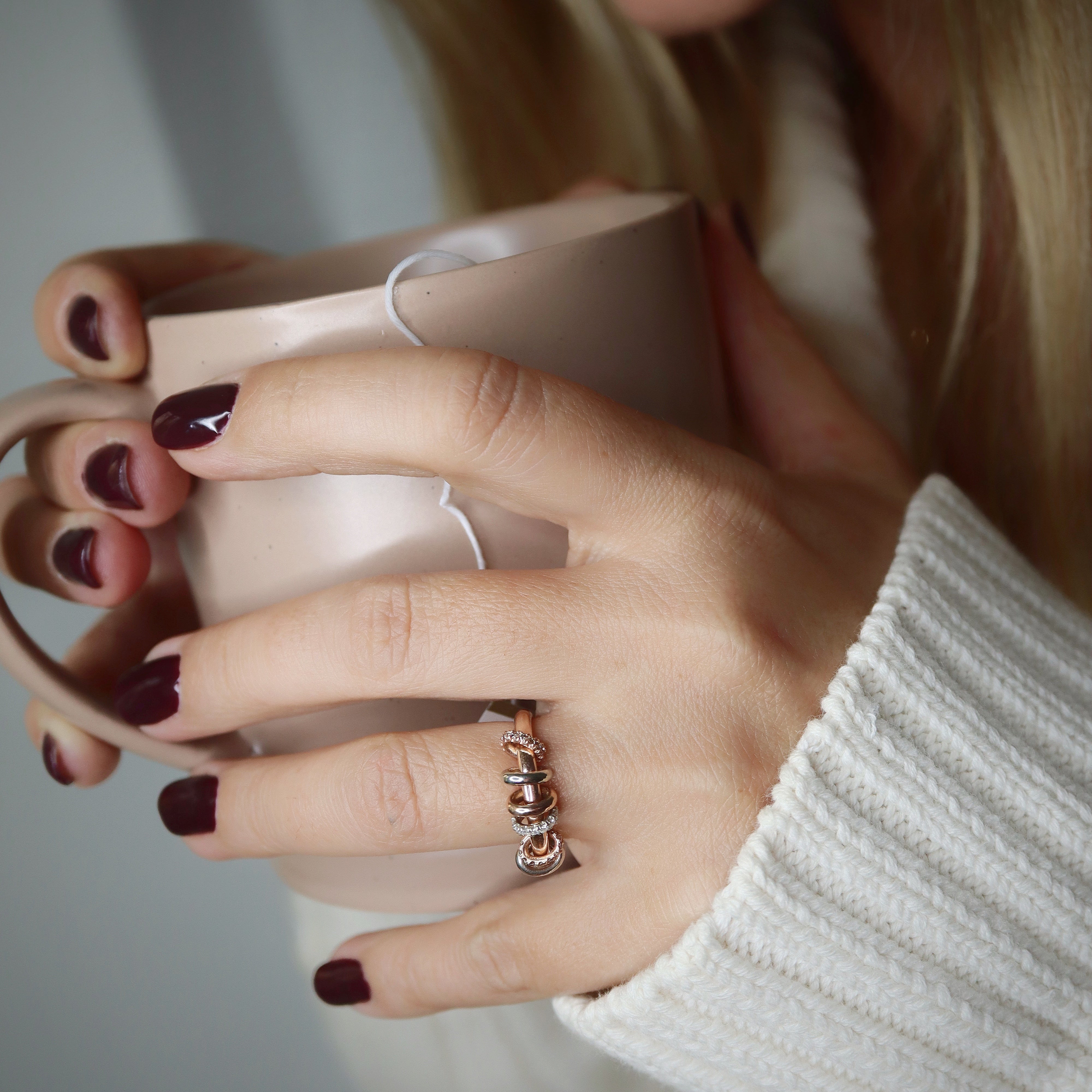 Close-up of a person wearing a multi gold band ring holding a pink mug with a blurred background