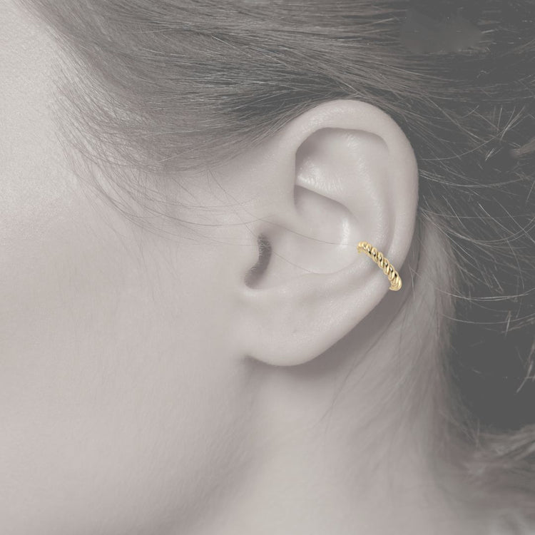 Close-up of an ear wearing a gold ear cuff rope design with a blurred background